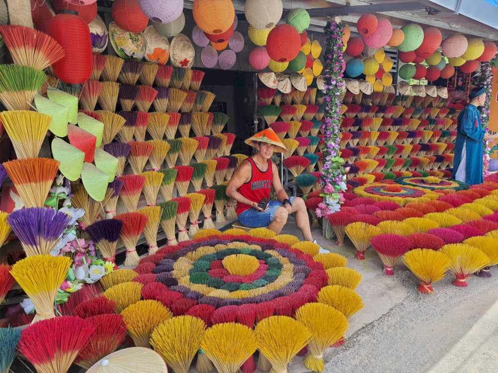 A traveler wearing non la poses amidst a sea of colorful incense sticks in Thuy Xuan Village 